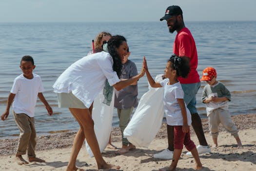A diverse group of volunteers, including children and adults, clean up a beach and celebrate with high-fives.
