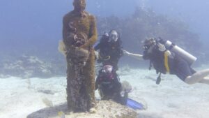 Divers exploring an underwater museum in Isla Mujeres, capturing marine life art.