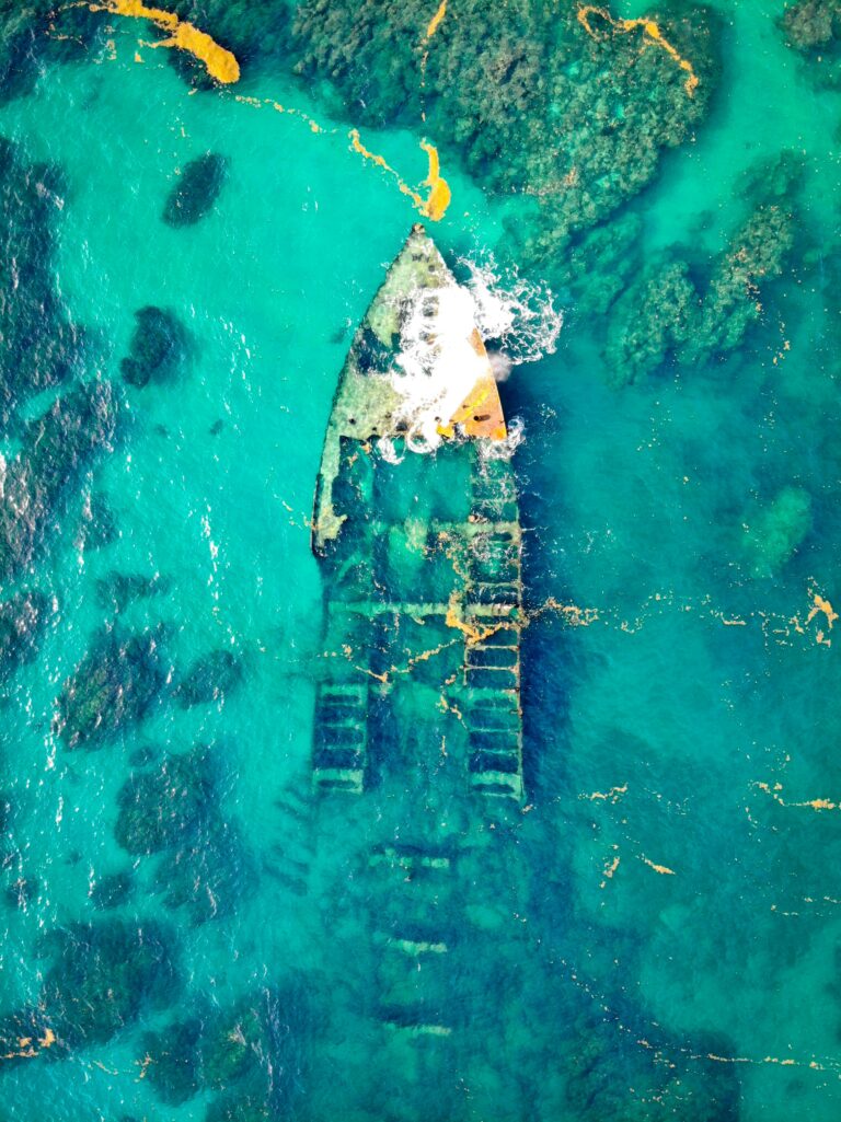 Drone captures stunning aerial shot of a sunken ship in crystal clear waters, revealing intricate details.